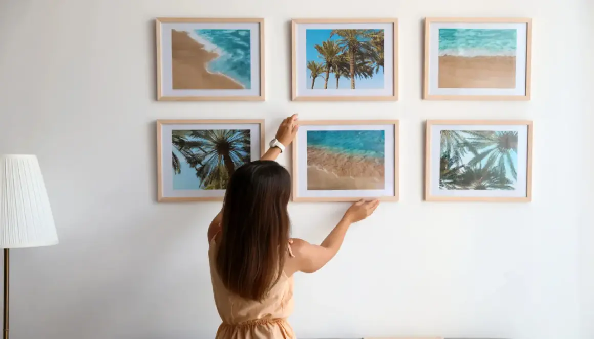 Frau arrangiert Bilder mit Strandmotiven. Tolle bilder anordnen ideen für eine sommerliche Wandgestaltung.