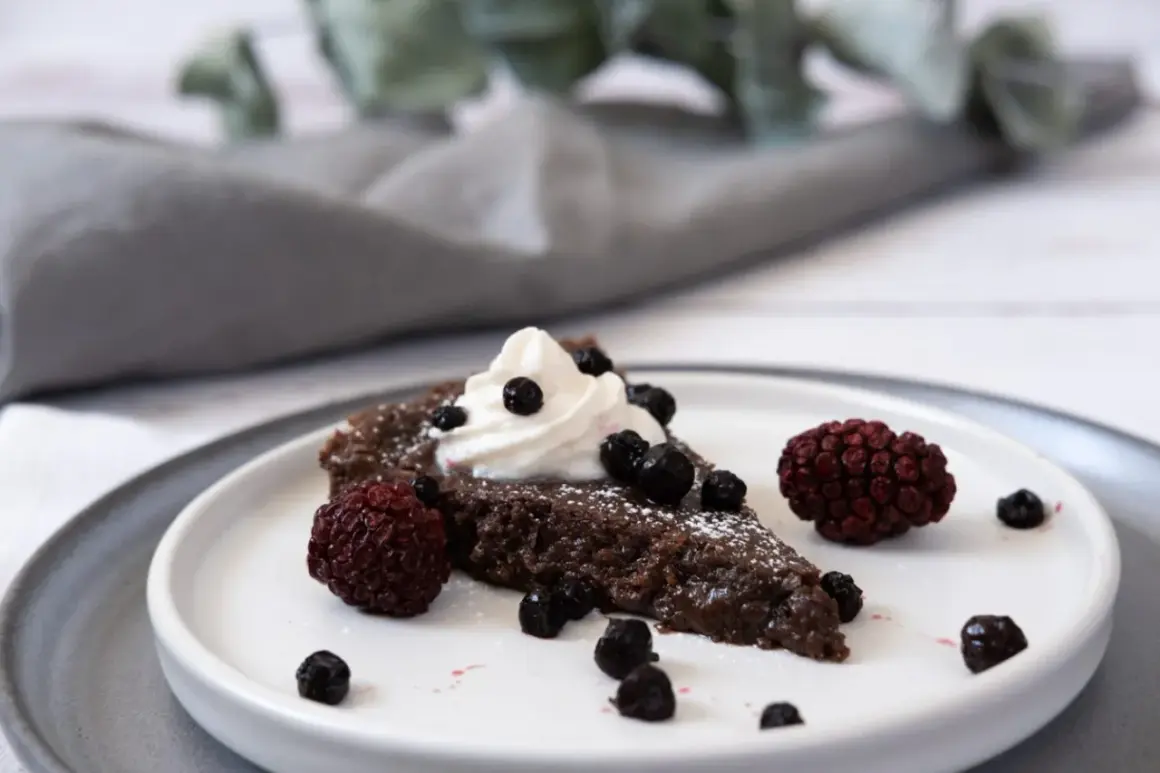 En bit vegansk kladdkaka med vispad grädde och bär.