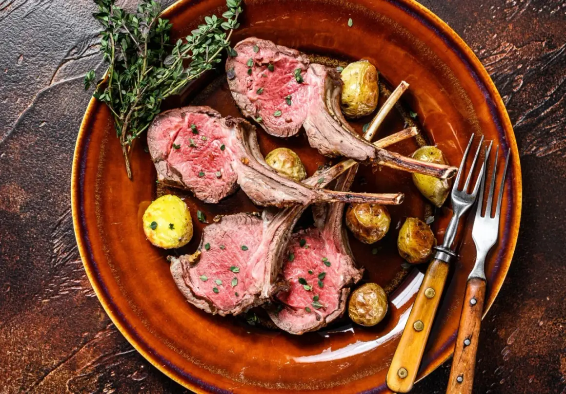 Costolette di agnello in padella, succulente e rosate, servite con patate novelle arrosto e rametti di timo su un piatto di terracotta.