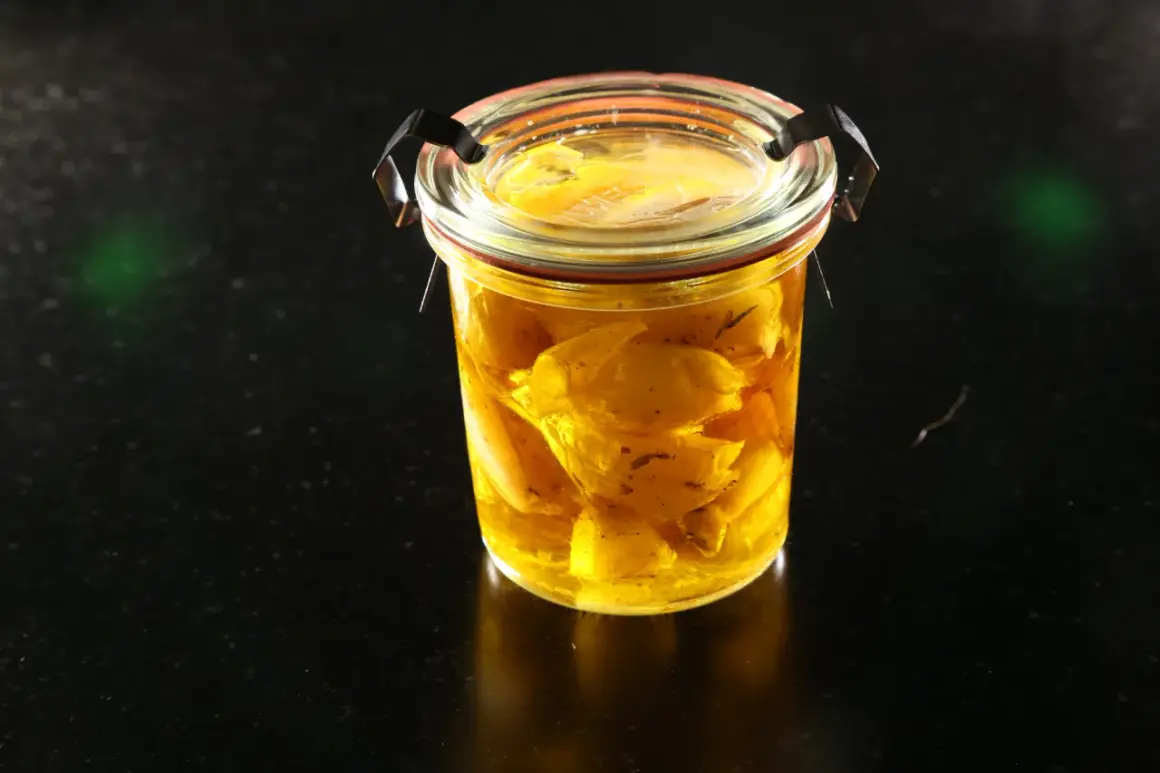 Un bocal en verre rempli d'ail confit dans de l'huile dorée. Les bienfaits de l'ail confit sont nombreux pour la santé.