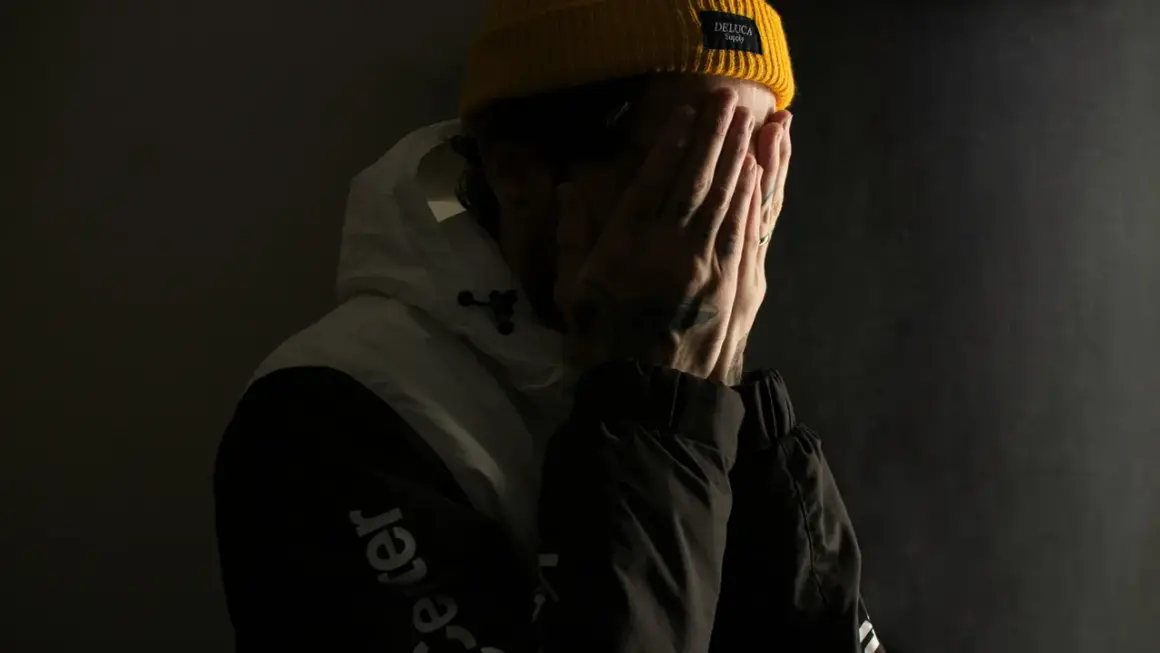 Ein Mann mit gelber Mütze verdeckt sein Gesicht mit den Händen, als ob er mit seinem Gewissen ringt.