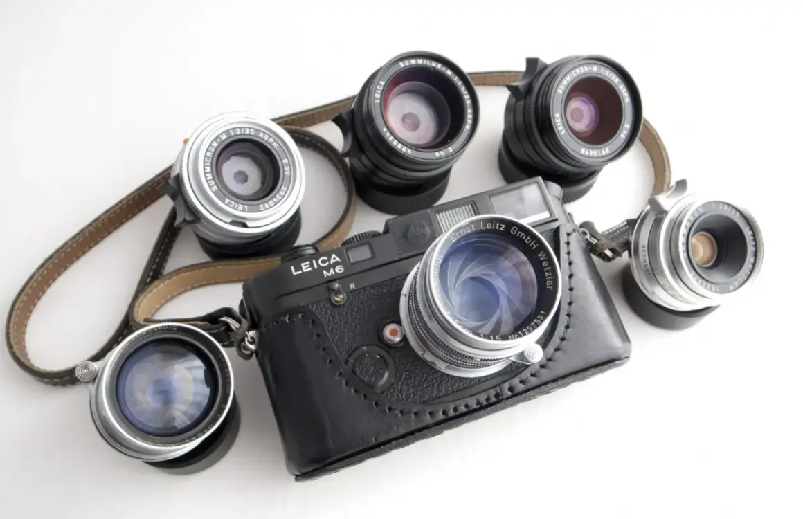 A Leica M6 camera with a leather case is surrounded by several best M mount lenses, showcasing a collection of classic photographic gear.