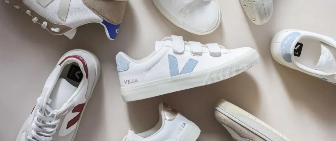 Plusieurs baskets Veja blanches, certaines avec des touches de couleur, sont disposées sur un fond clair. Idéal pour apprendre comment nettoyer des baskets.