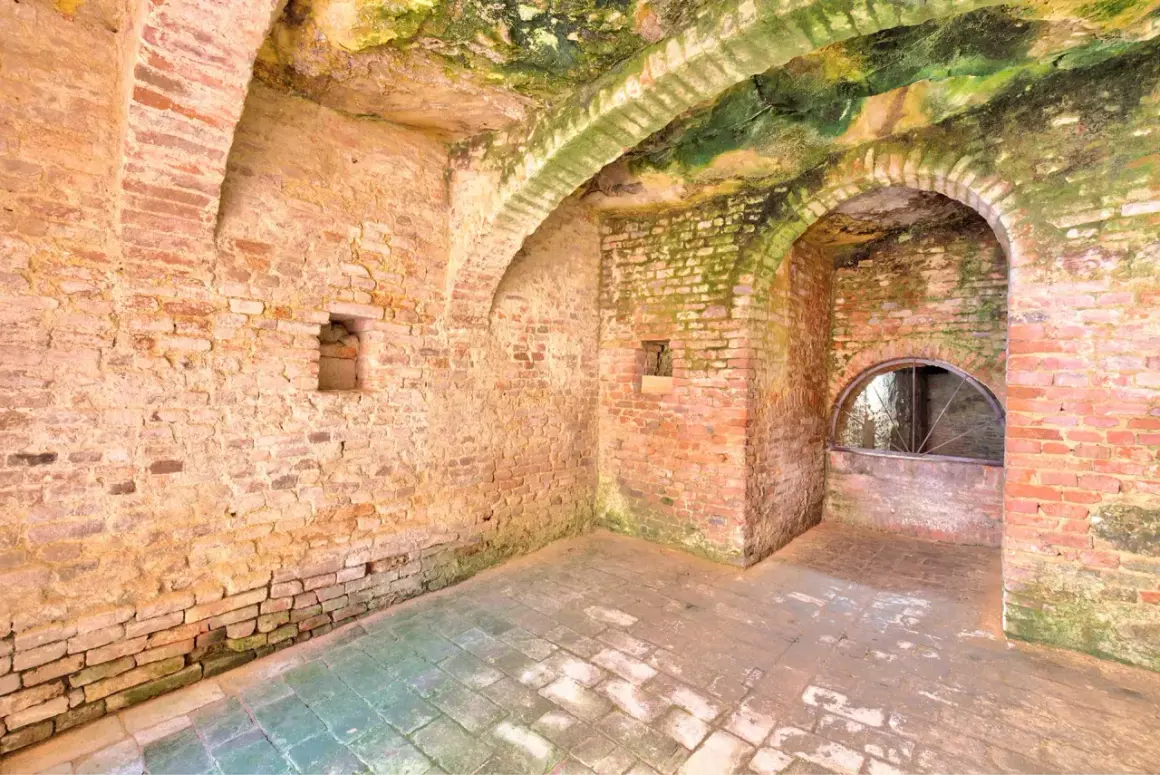 Interno di Santa Maria a Monte: muri in mattoni grezzi, volte muschiose e un arco con una finestra semicircolare.