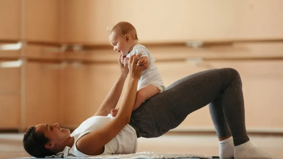 Une mère fait des exercices pour renforcer son périnée après accouchement, soulevant son bébé joyeux.