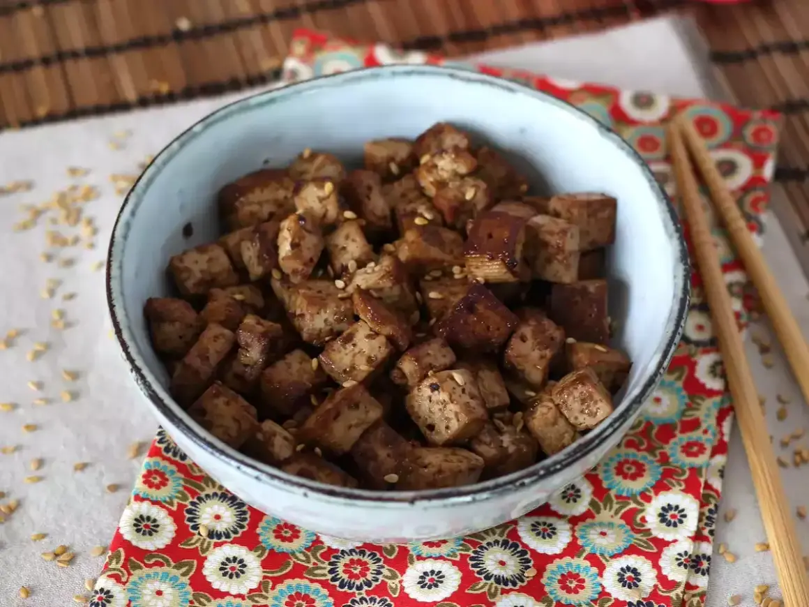 En skål med krispiga, tärnade tofu bitar, glaserade i en smakrik, glutenfri marinad och toppade med sesamfrön.