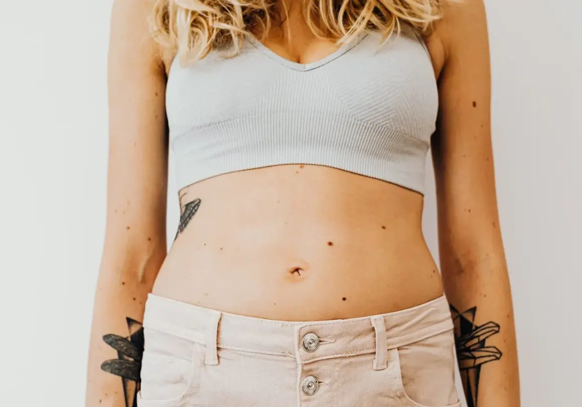 En kvinna med tatueringar på armarna och magen, som visar sin mage som kan vara känslig för gluten.
