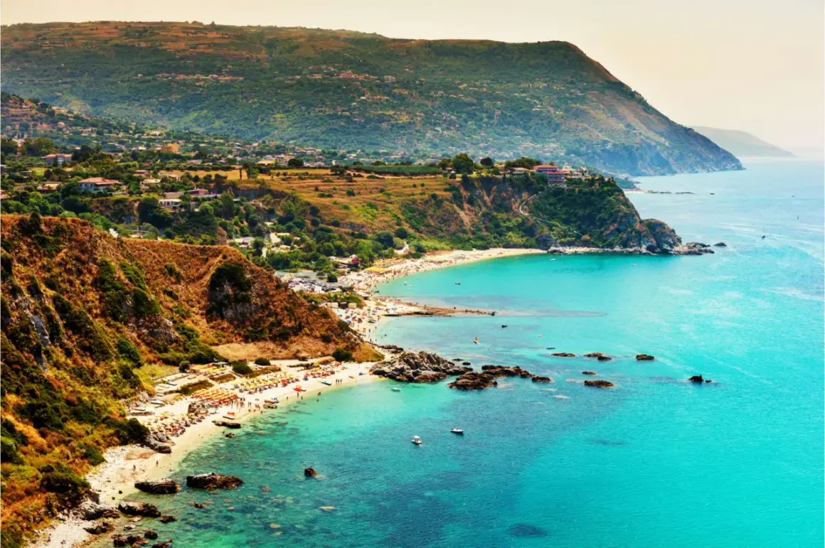 Vista mozzafiato del capo Vaticano a Tropea, con il mare cristallino che lambisce le spiagge affollate e le scogliere verdi.