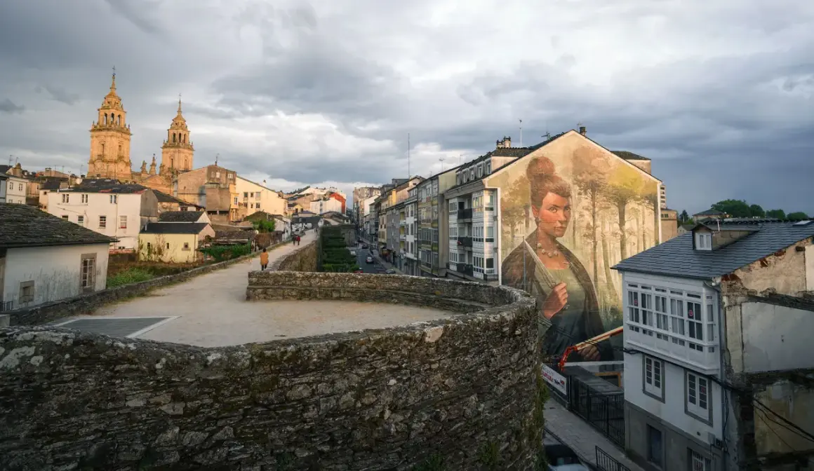 Mural de una mujer en la muralla de la fortaleza Lugo, con la catedral al fondo y un cielo nublado.
