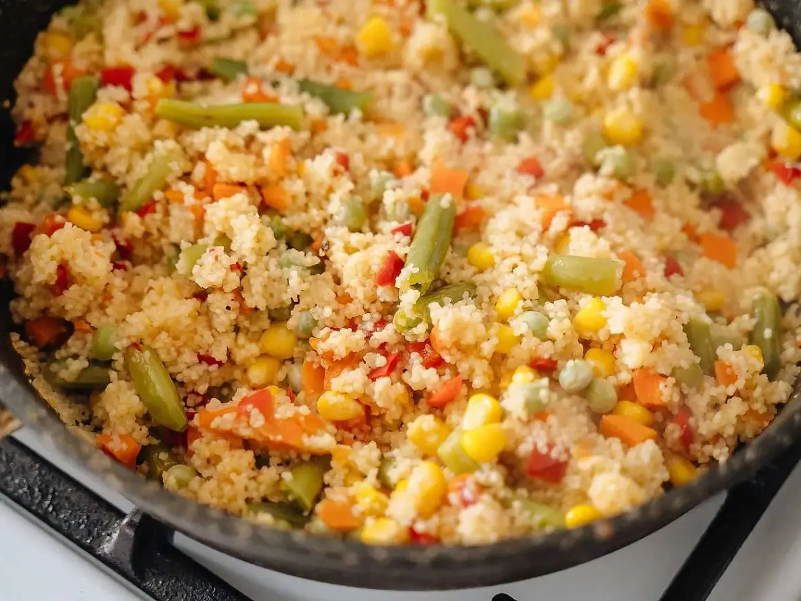 En varm och färgglad couscousrätt med gröna bönor, majs, morötter och paprika i en stekpanna.