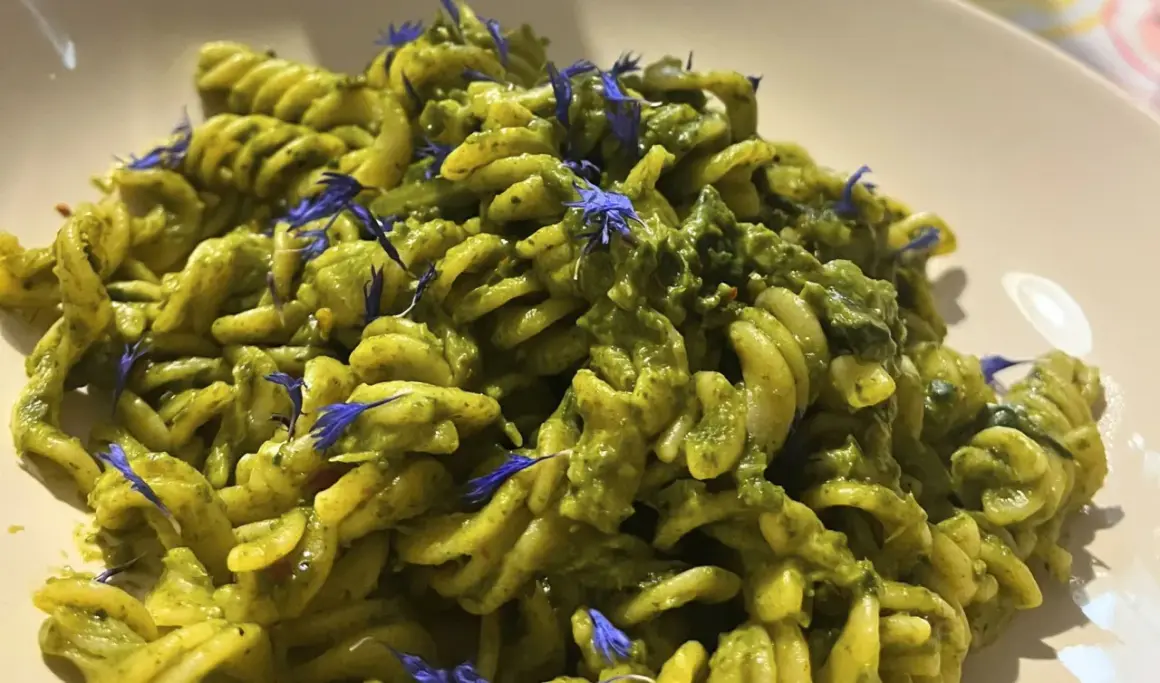 Fusilli-Pasta mit einer cremigen grünen Soße, garniert mit blauen Kornblumen. Ein köstliches italienisches Palmkohl Rezept.