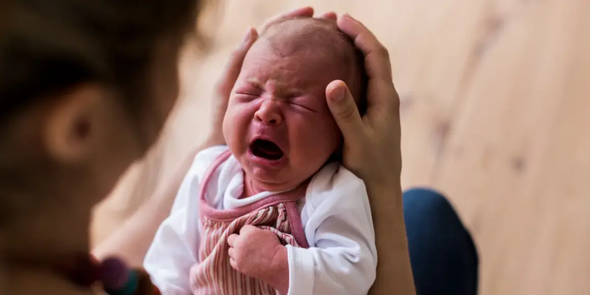 Ein Neugeborenes schreit laut, während es von Eltern gehalten wird. Die Frage, warum schreien Babys nach der Geburt, beschäftigt viele.