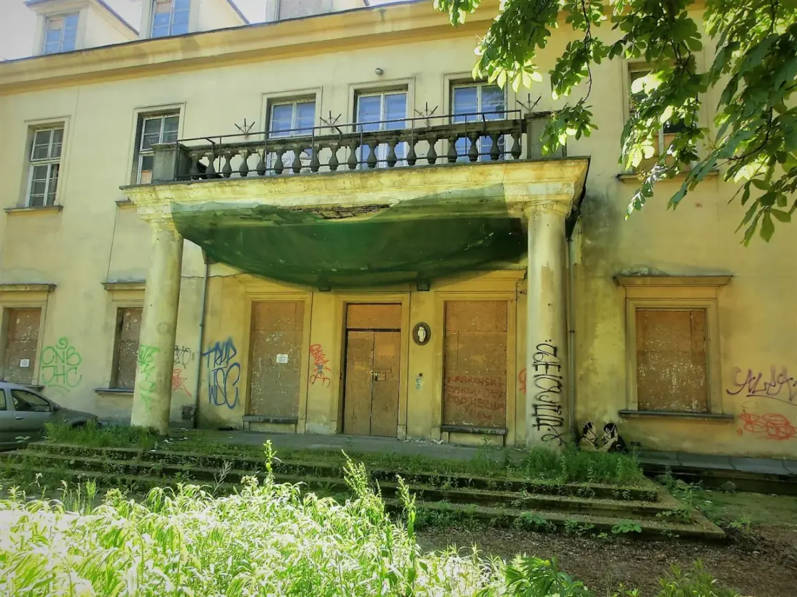 Zaniedbany pałac Tarnowskich w Krakowie, z zabitymi deskami oknami i drzwiami, pokryty graffiti.