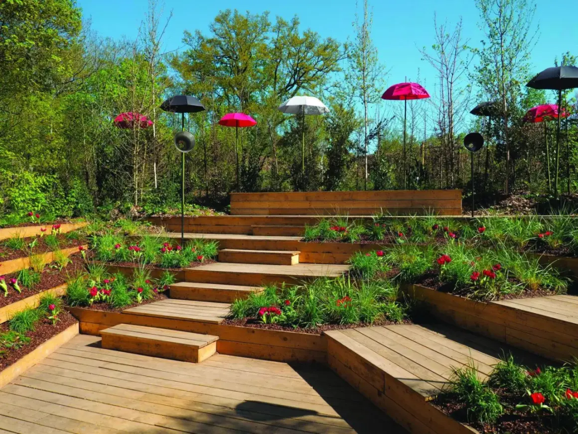 Escalier extérieur en bois avec des parterres de fleurs et des parasols colorés. La norme hauteur marche escalier extérieur est respectée pour un accès sûr.