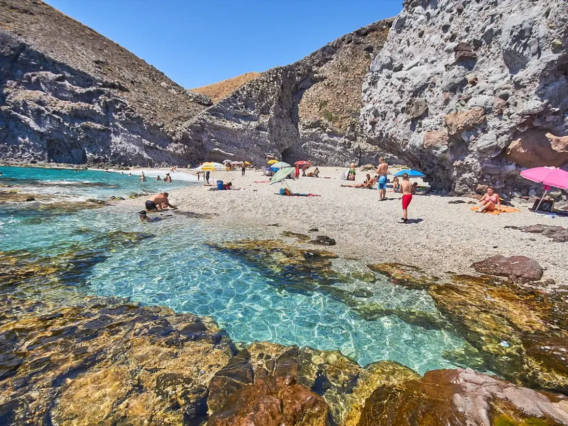 Descubre qué ver en Carboneras: una cala rocosa con aguas cristalinas y gente disfrutando del sol y el mar.