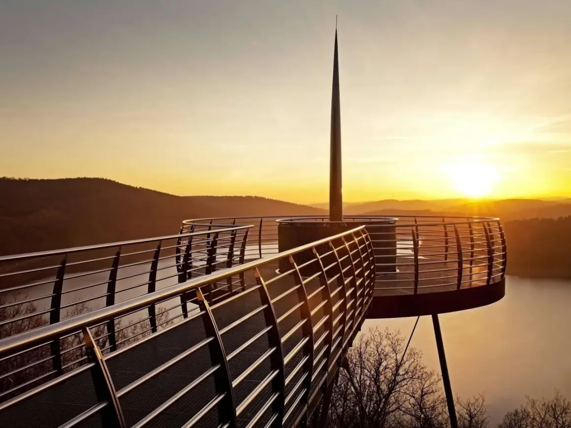 Ein Skywalk NRW bei Sonnenuntergang mit Blick auf einen See und bewaldete Hügel.