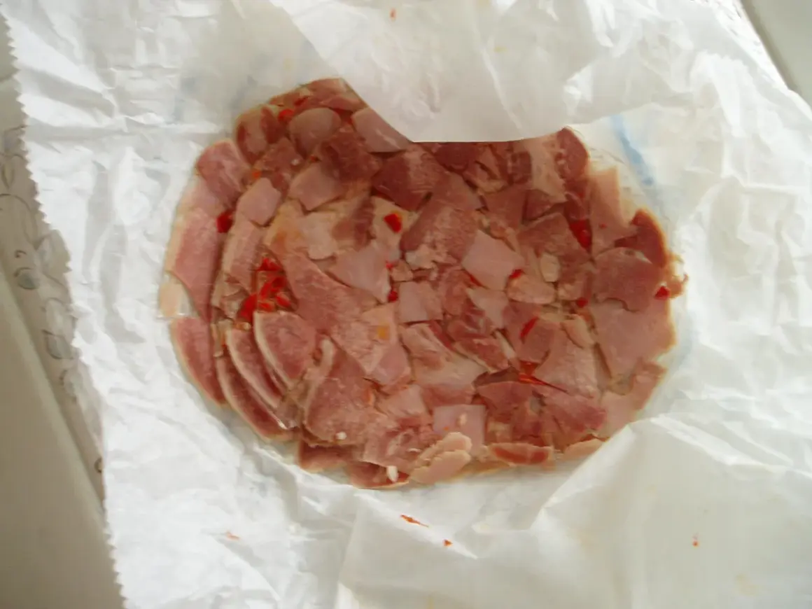Rebanadas de queso de cabeza con trozos de pimiento rojo, envueltas en papel blanco.