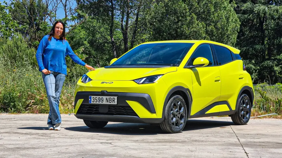 Mujer sonriente junto a un BYD Dolphin de vibrantes **colores** amarillos, destacando su diseño moderno en un entorno natural.