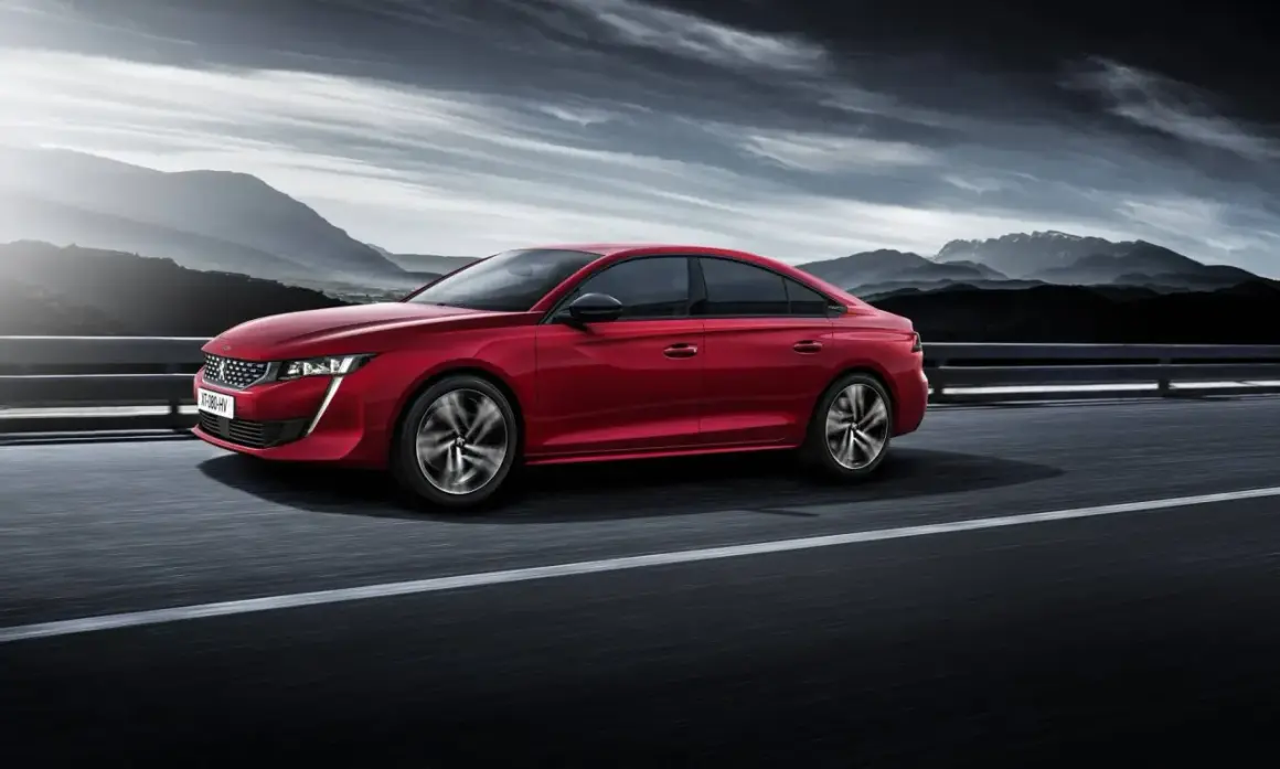 Voiture rouge Peugeot 508, un modèle à éviter, roulant sur une route avec des montagnes en arrière-plan sous un ciel dramatique.