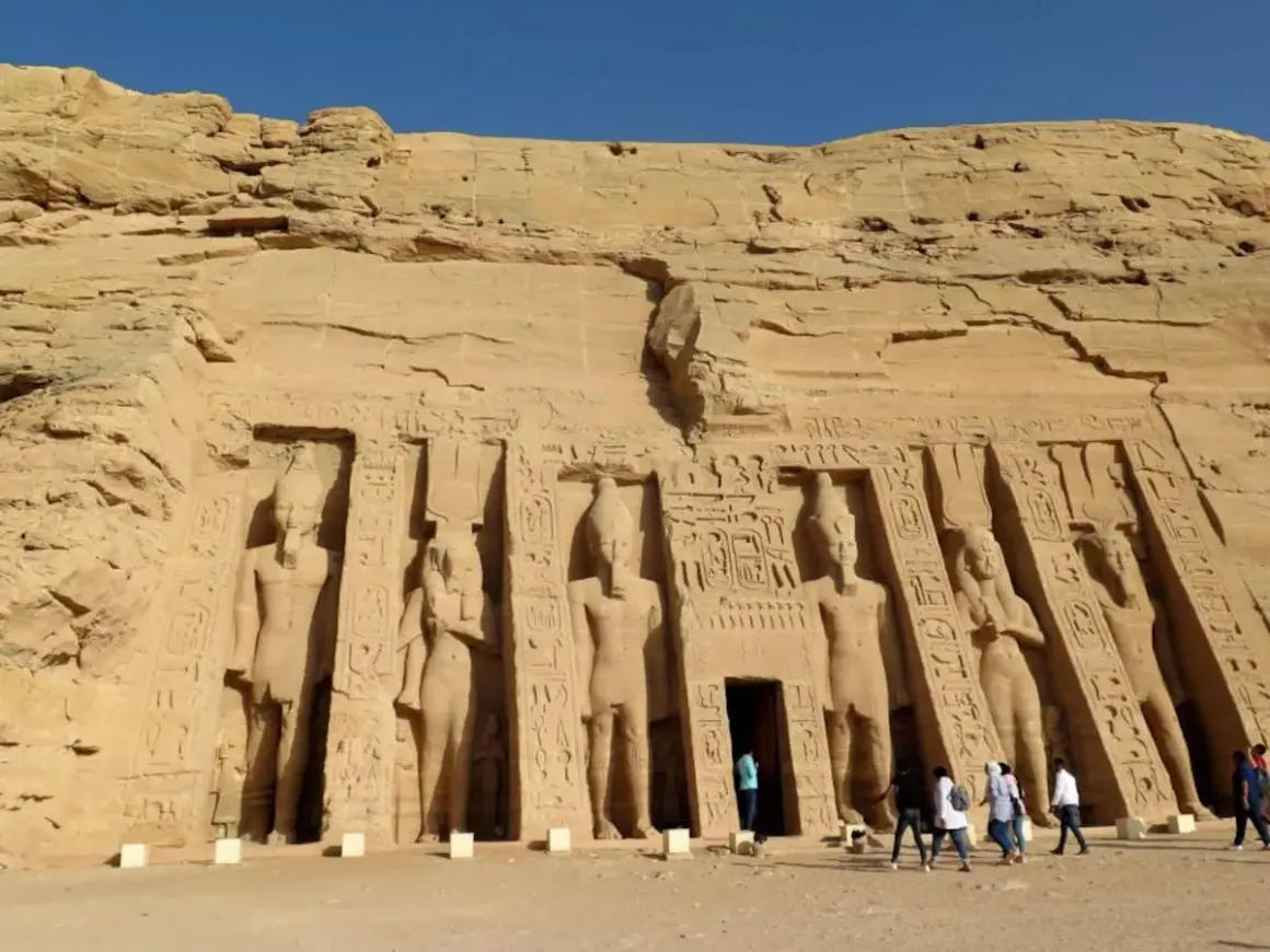Gigantescas estatuas talladas en la roca flanquean la entrada del templo de Abu Simbel. Turistas admiran la majestuosidad de este sitio histórico.
