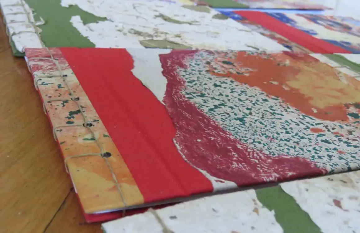 Dettaglio di come rilegare fogli a mano con filo, creando un quaderno artistico con copertina colorata.