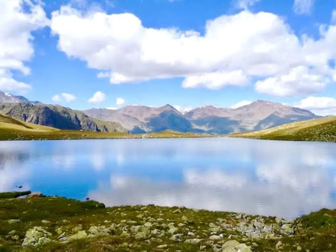Un sereno lago alpino riflette il cielo azzurro e le montagne. Un paesaggio da sogno nel Trentino.