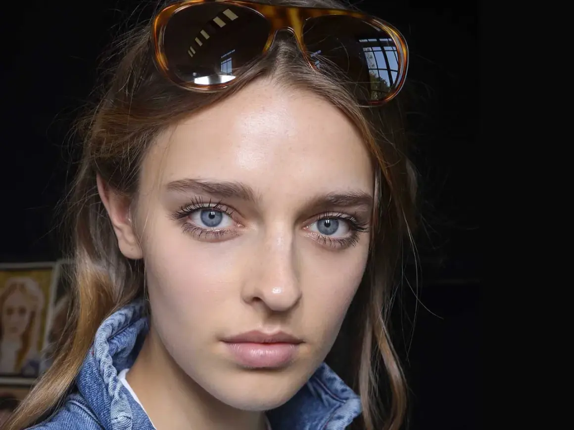 Ragazza con occhiali da sole in testa, viso illuminato da fondotinta e fard, ciglia lunghe e occhi azzurri.