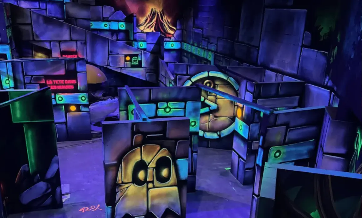 Labyrinthe de laser game aux couleurs vives, avec des fantômes et un volcan en arrière-plan. Le panneau "LA TÊTE DANS LES NUAGES" suggère une expérience amusante.