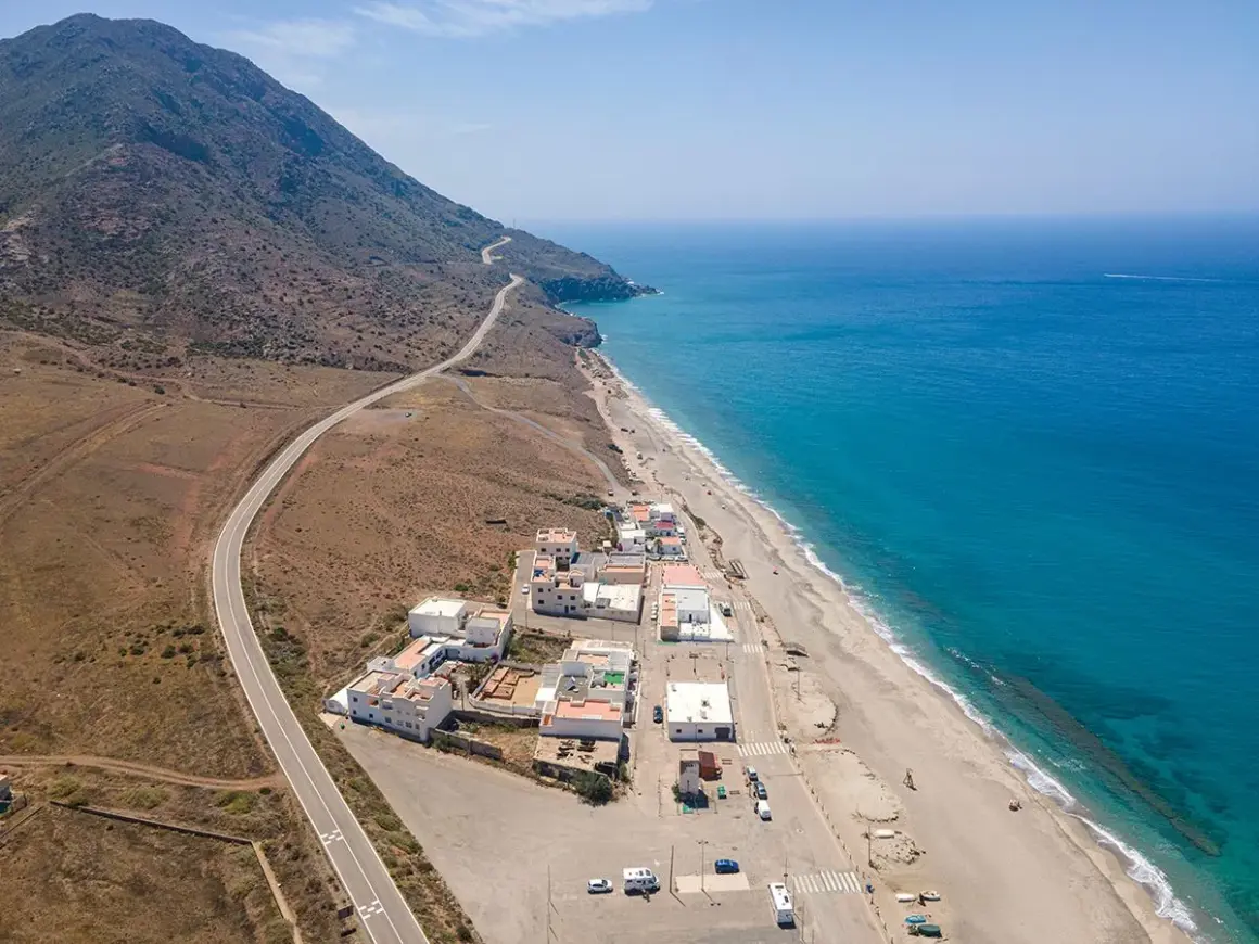 Vista aérea de la playa de la Almadraba en Almería, con el mar azul intenso, la arena dorada y un pueblo costero.