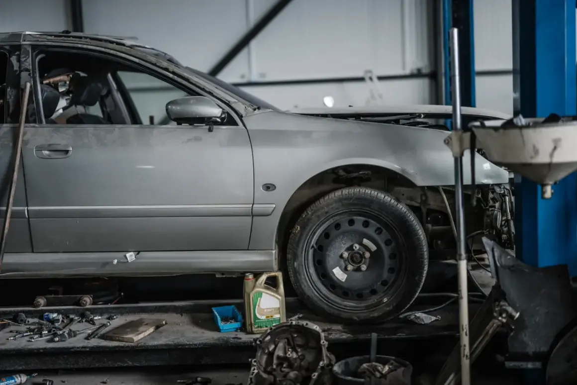 Voiture argentée en réparation dans un garage, avec des outils et une boîte d'huile. Le frein à main est prêt pour le prochain contrôle.