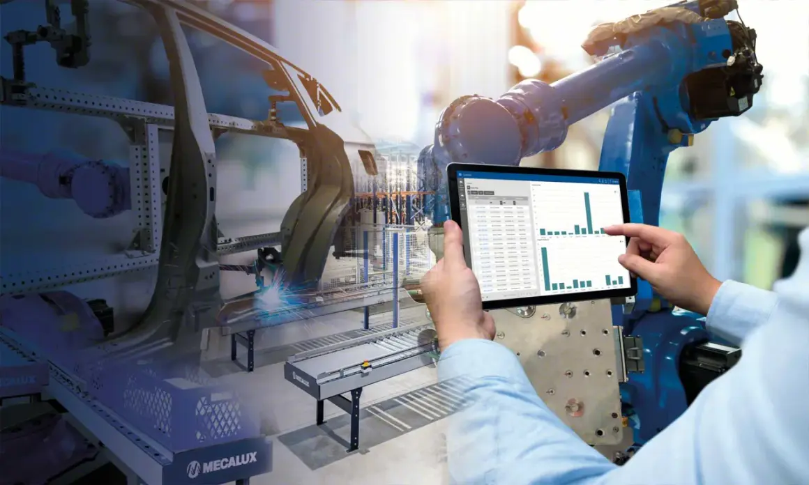 Ręka wskazuje na tablet z danymi produkcyjnymi, podczas gdy robot spawa karoserię samochodu. To przykład strategii push w nowoczesnej fabryce.
