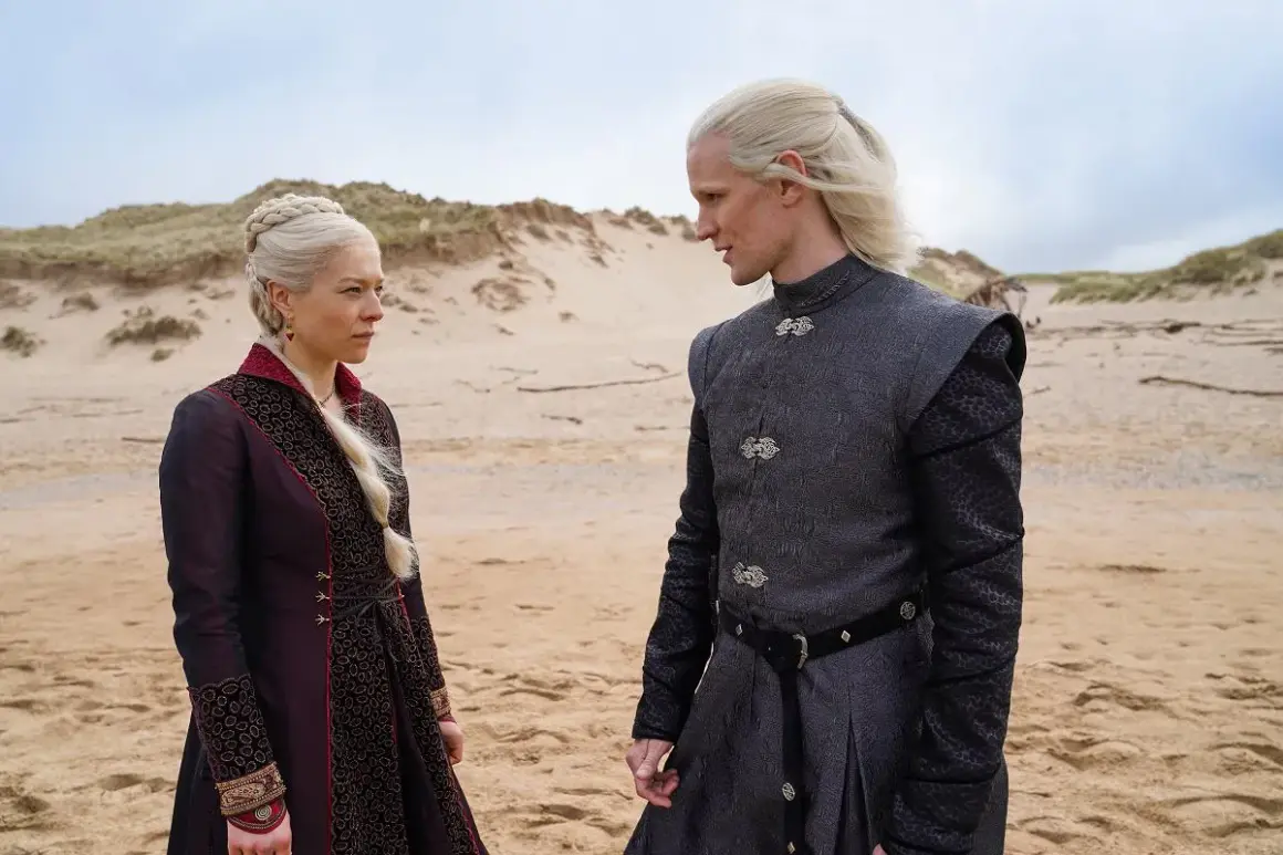 Rhaenyra i Daemon Targaryenowie, bohaterowie "Ród smoka", stoją na piaszczystej plaży, wpatrzeni w siebie.