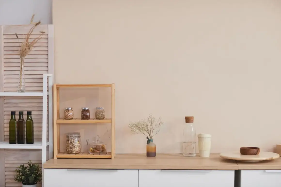 Regale mit Vorräten, Ölflaschen und Pflanzen zeigen **minimalismus im alltag**. Eine Vase mit Trockenblumen und eine Wasserflasche ergänzen die Szene.