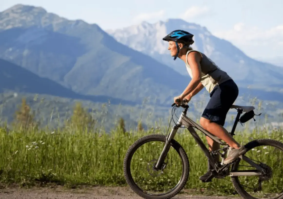 Ciclista sonriente pedalea por un camino de grava con montañas al fondo. Una aventura de pirinexus gravel.
