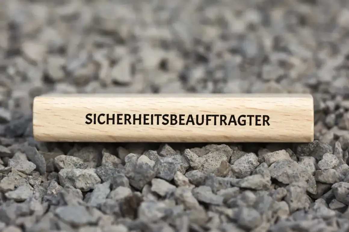 Ein Holzstab mit der Aufschrift "SICHERHEITSBEAUFTRAGTER KITA" liegt auf grauem Schotter.