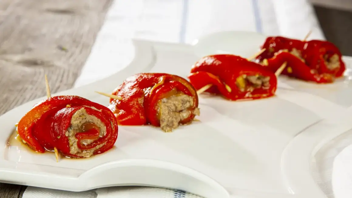 Peperoncini ripieni alla piemontese, rotolini rossi con ripieno saporito, serviti su un piatto bianco.