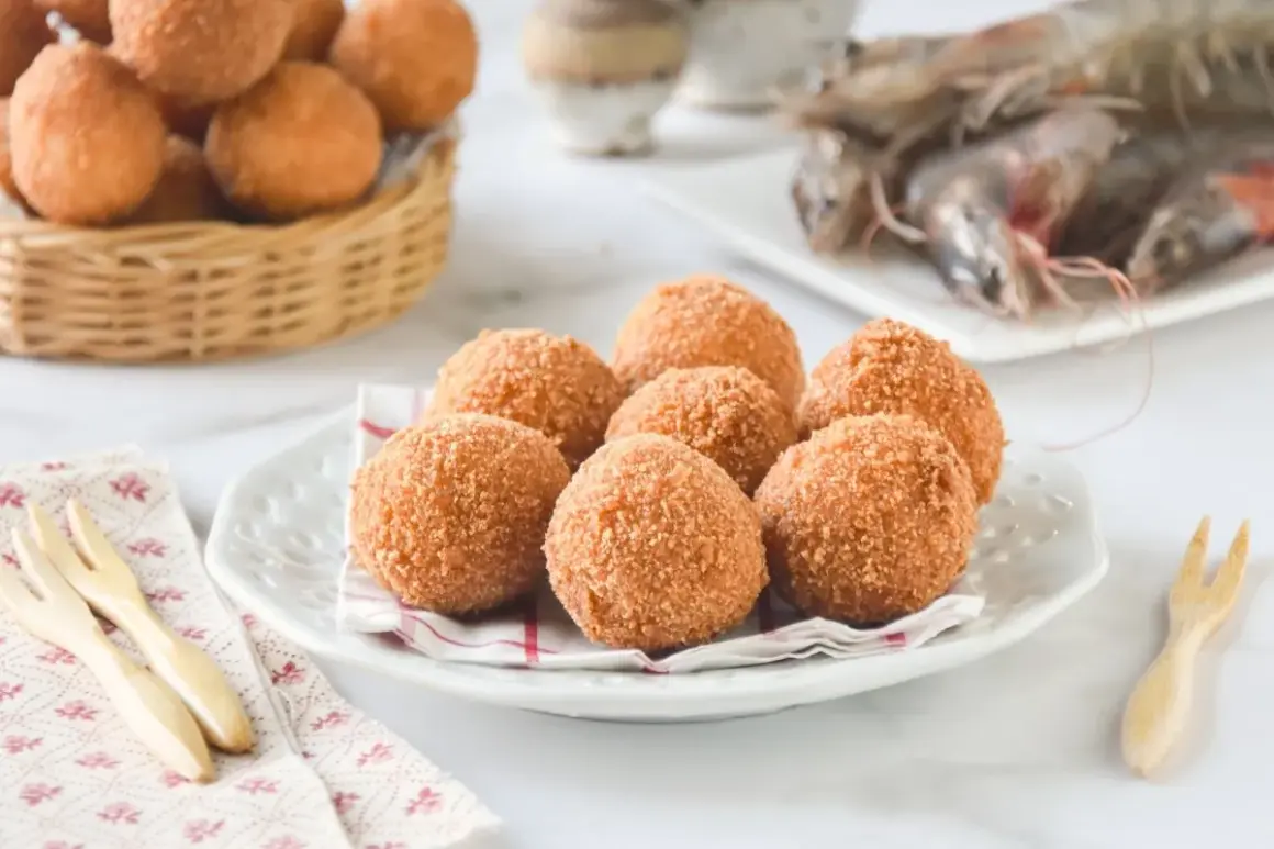 Croquetas de gambas doradas y crujientes en un plato, con gambas crudas al fondo.