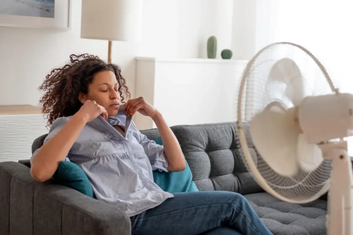 Frau in 40. SSW kämpft mit Hitzewallungen, versucht sich mit einem Ventilator Linderung zu verschaffen.