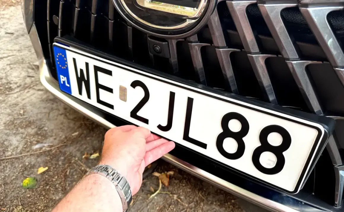 Dłoń poprawia tablicę rejestracyjną z numerem WE 2JL88, przygotowując wniosek o rejestrację pojazdu.