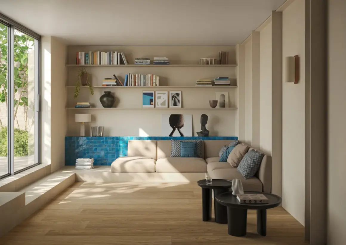 Ein heller Boden trifft auf eine warme, sandfarbene Wandfarbe. Ein gemütliches Wohnzimmer mit Bücherregalen, einem Sofa und einem großen Fenster.