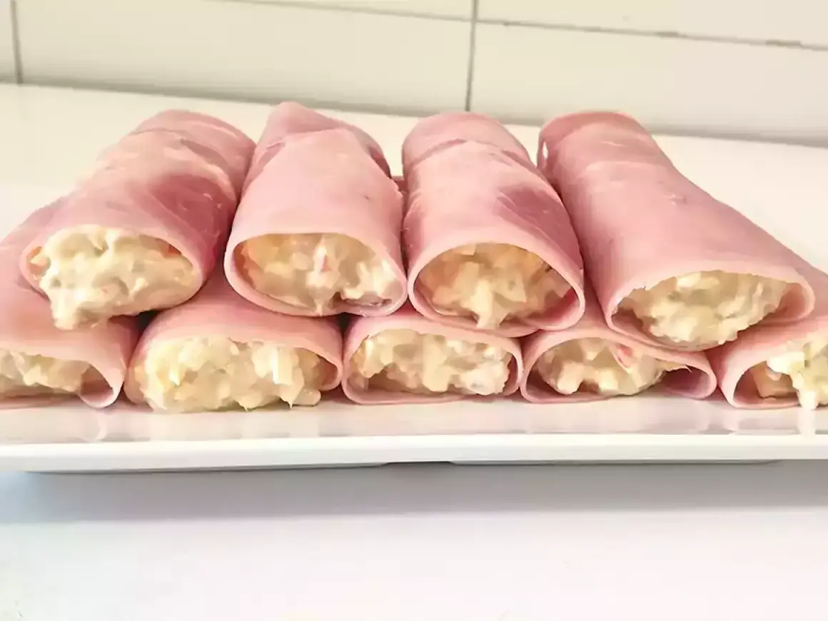 Rollitos de jamón york rellenos de ensaladilla cremosa, presentados en una bandeja blanca.