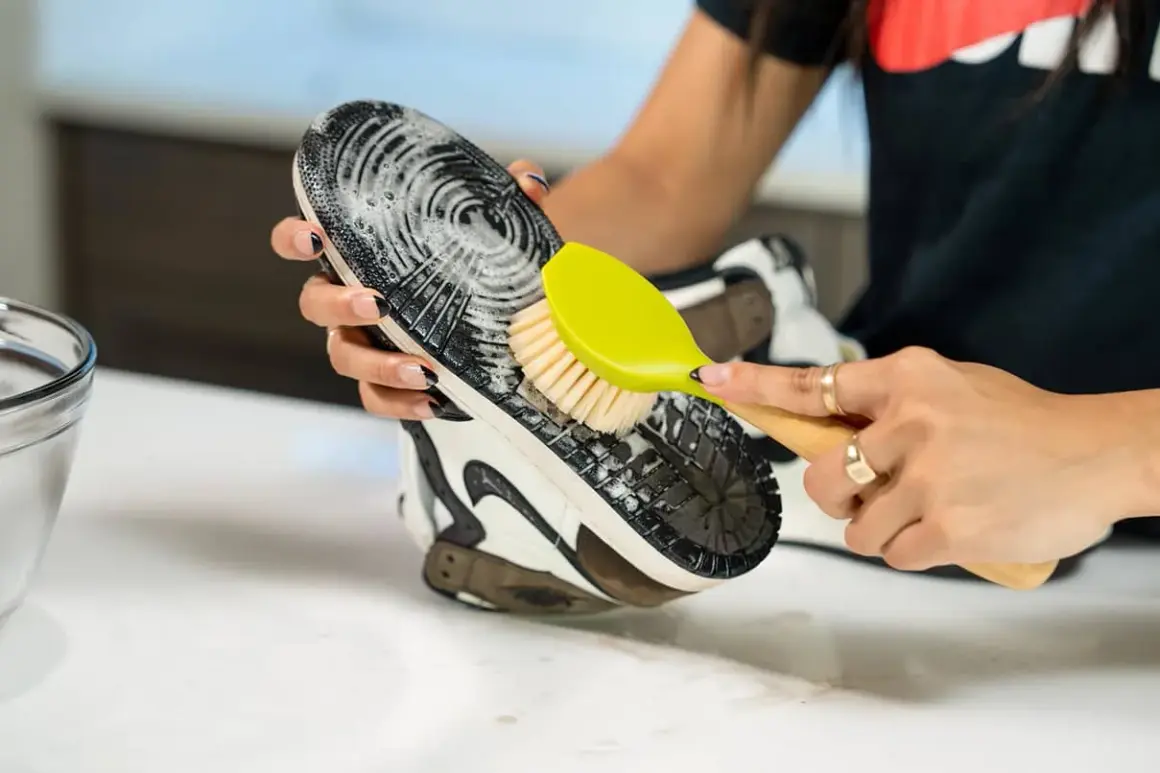 Main tenant une brosse verte, une personne nettoie la semelle extérieure d'une chaussure avec de la mousse.