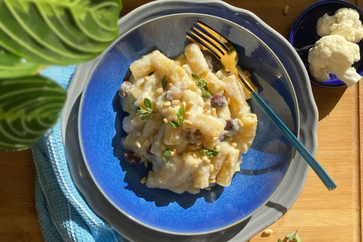 Creamy pasta with cauliflower, pine nuts, and herbs on a blue plate with a gold fork.