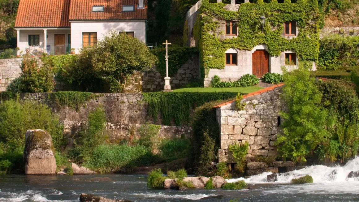 El pazo de Ponte Maceira, con su arquitectura de piedra y vegetación exuberante, se alza junto a un río de aguas bravas.