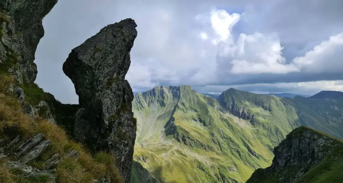 Steile Felsformationen und grüne Berghänge im Rahmen einer **Karpaten Wanderung**. Dramatische Wolkenformationen über den Gipfeln.