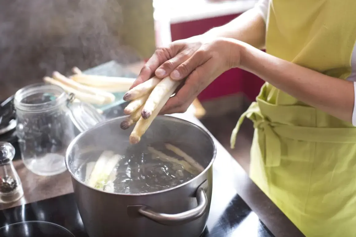 Hände legen weißen Spargel in kochendes Wasser. So wird gefrorener Spargel kochen.