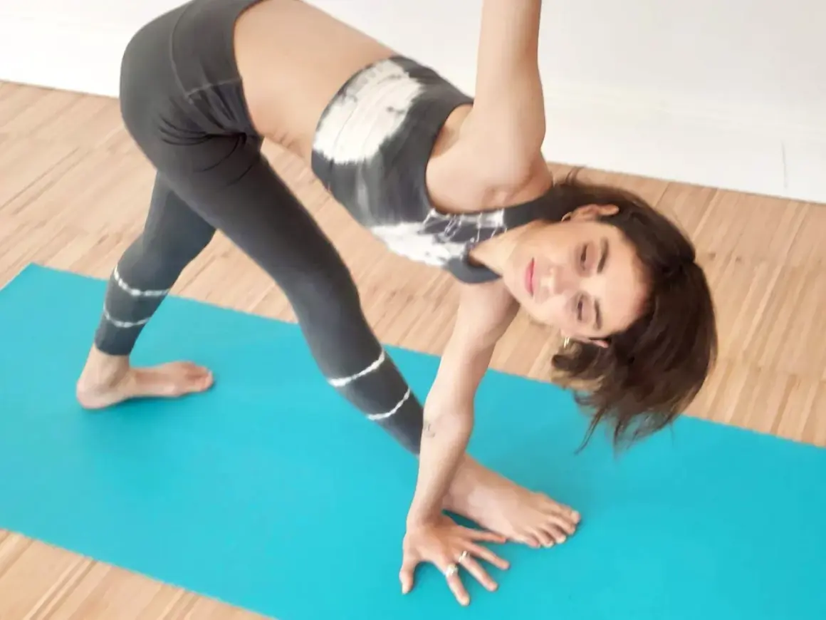 Mujer practicando torsiones yoga en una esterilla azul. Su cuerpo está girado, con una pierna extendida y la otra flexionada.
