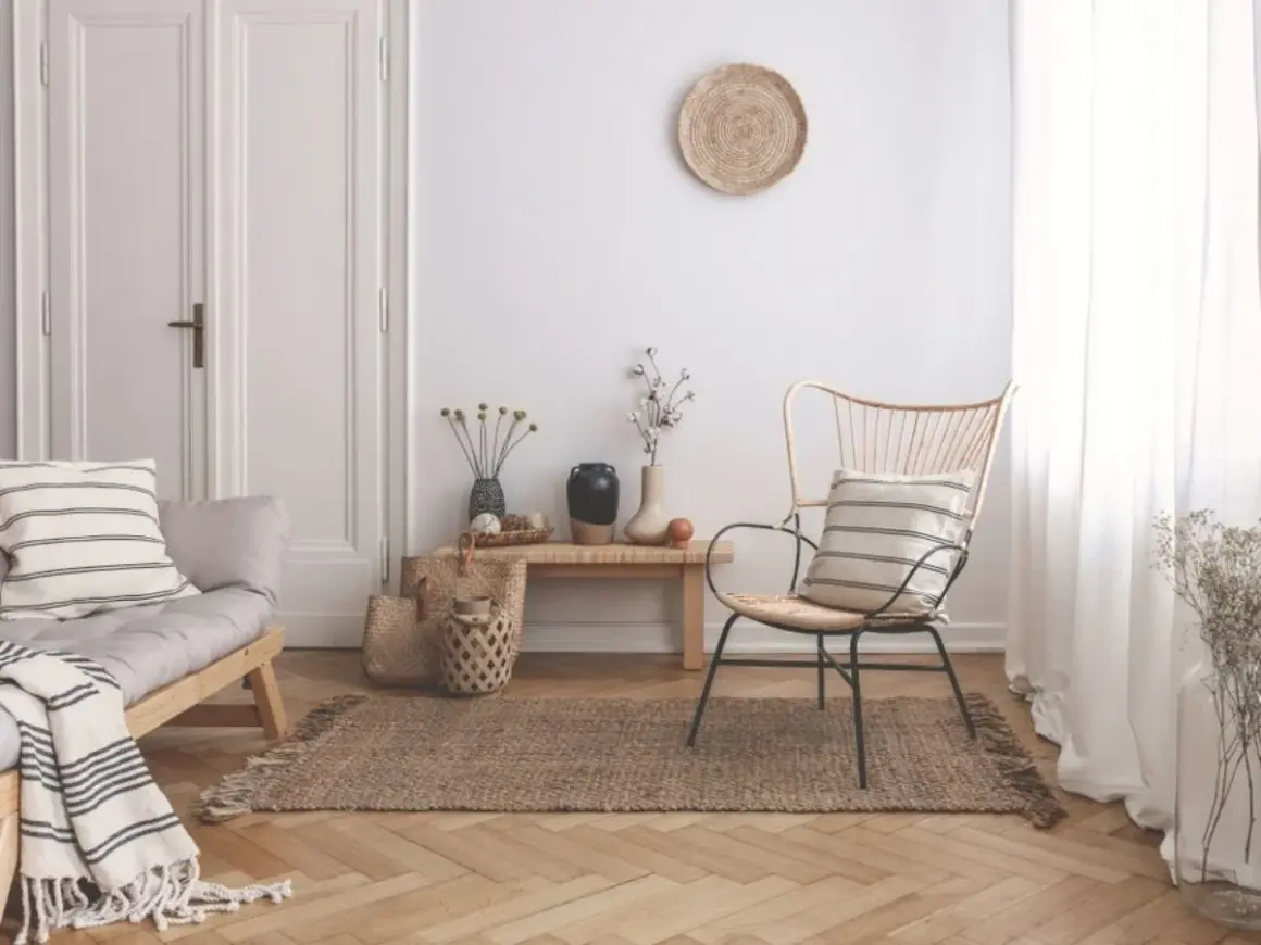 Un angolo del salotto arredato con un divanetto in legno, una poltrona in rattan, tappeto in juta e decorazioni naturali. Ecco come riempire un angolo del salotto con stile.