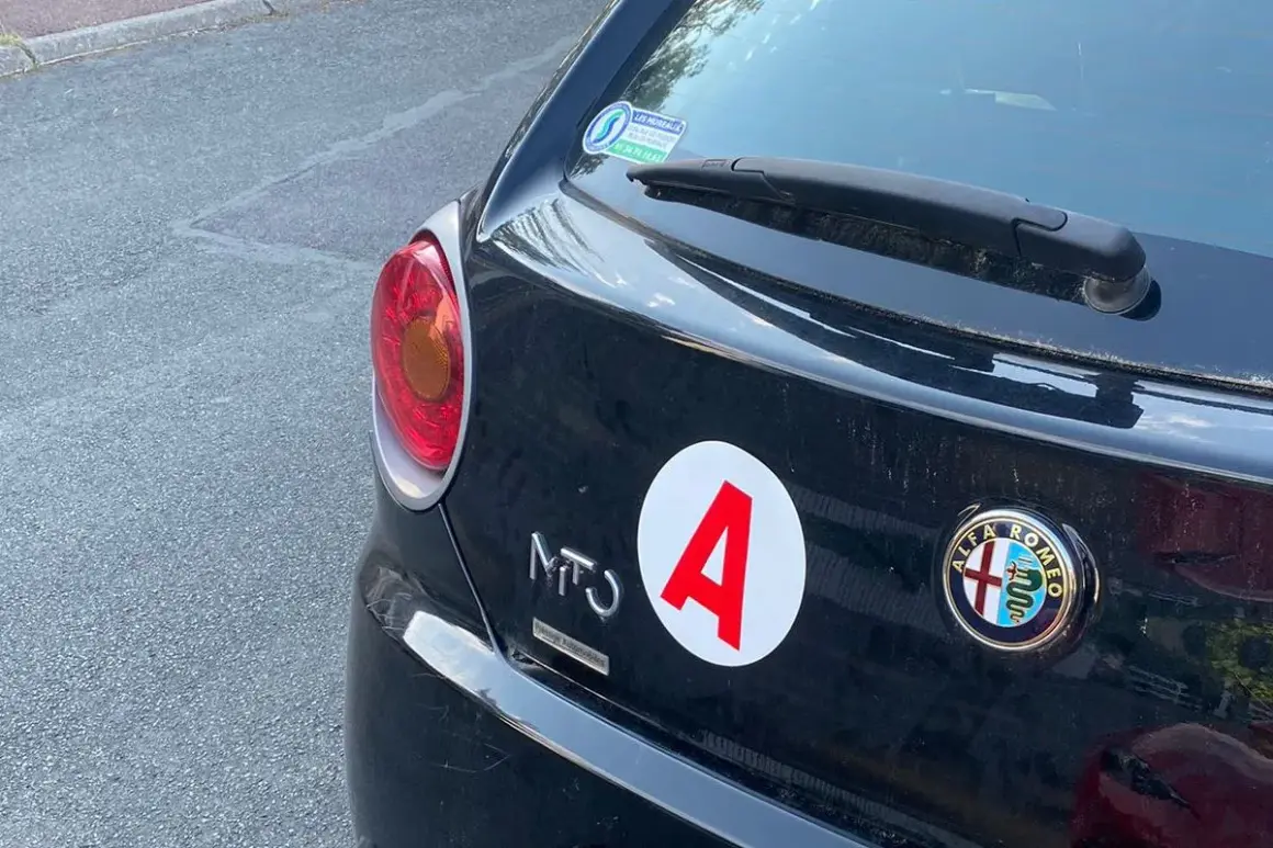 Autocollant "A" sur une Alfa Romeo noire, signe d'un jeune conducteur. La voiture a 140 ch.