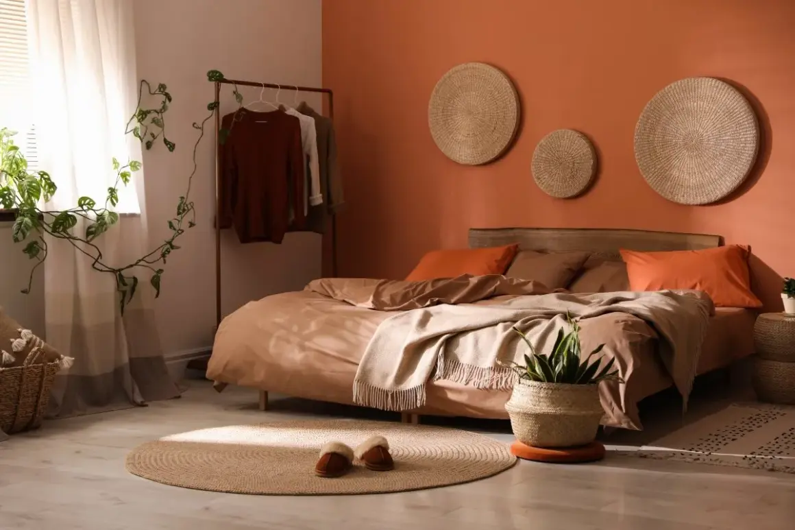 A cozy bedroom with bold colors like terracotta and rust. A bed with earthy-toned linens, a plant, and woven wall art.